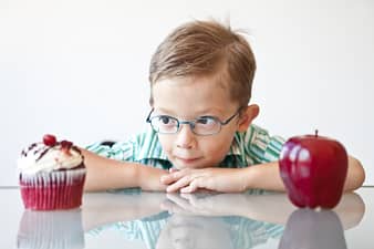 A little boy choosing between a cupcake and apple... Looks like the cupcake is the winner.